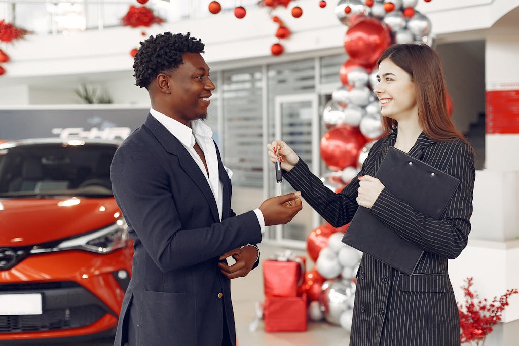 A car dealer handing over keys to a satisfied customer at a decorated dealership.